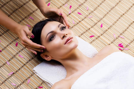Beautiful, young and healthy woman on bamboo mat in spa salon having temple massage. Spa, health and healing concept.の写真素材