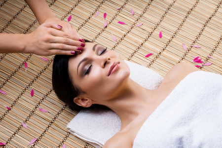 Beautiful, young and healthy woman on bamboo mat in spa salon having face massage. Spa, health and healing concept.の写真素材