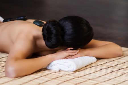 Beautiful, young and healthy woman on bamboo mat in spa salon is having hot stone massage. Spa, health and healing concept.の写真素材