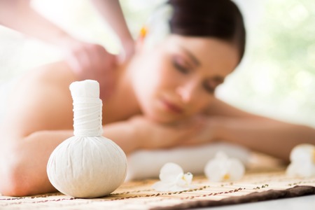 Young and beautiful girl relaxing in spa salon. Massage therapy over seasonal summer or spring background. Healing medicine and health care concept.の写真素材