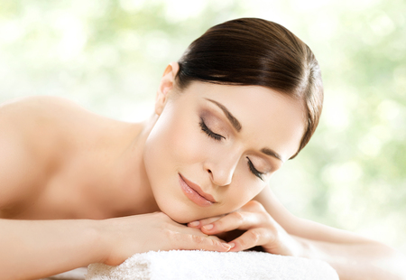 Young and beautiful girl relaxing in spa salon. Massage therapy over seasonal summer or spring background. Healing medicine and health care concept.の写真素材