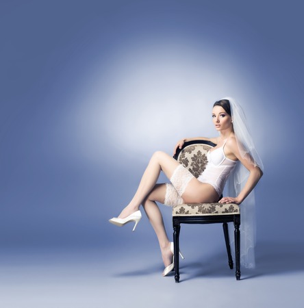 Young sexy bride in erotic lingerie over blue background. Sitting on a chair.の写真素材