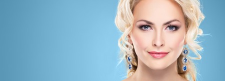 Beautiful blond girl with luxury golden necklace over blue background.の写真素材