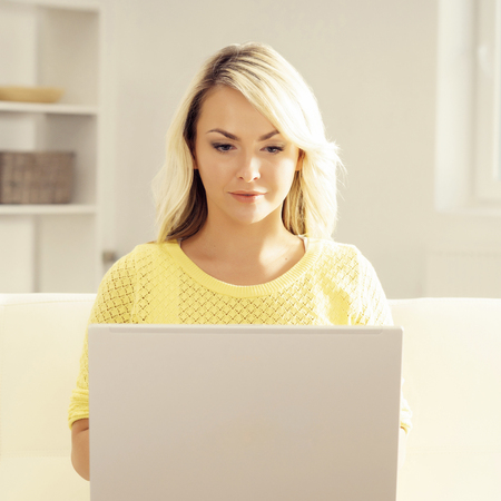 Happy blonde girl with notebook at home. Online shopping, laptop, computer concept.の写真素材