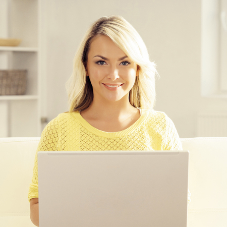 Happy blonde girl with notebook at home. Online shopping, laptop, computer concept.の写真素材