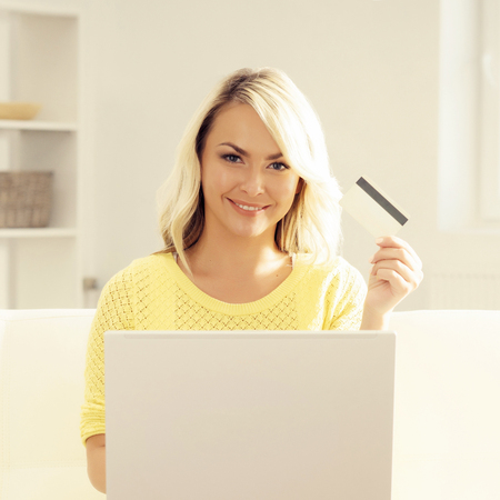 Happy blonde girl with credit card and notebook. Online shopping, laptop, computer concept.の写真素材