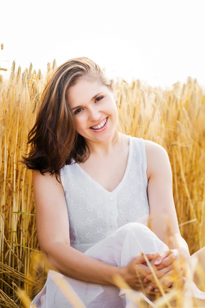 Young, emotional and happy woman in a meadow of rye. Beautiful girl in a white dress. Summer concept.の写真素材