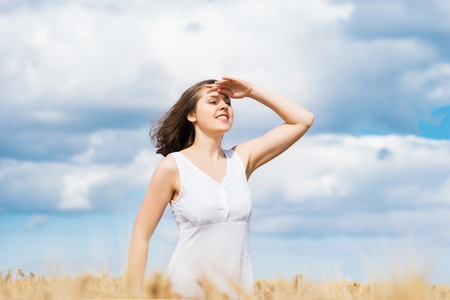 Young, emotional and happy woman in a meadow of rye. Beautiful girl in a white dress. Summer concept.の写真素材