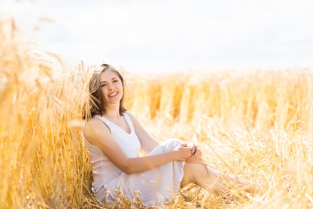 Young, emotional and happy woman in a meadow of rye. Beautiful girl in a white dress. Summer concept.の写真素材