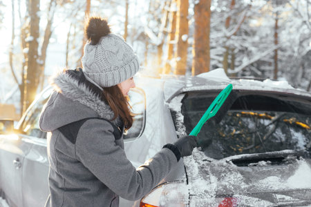 Happy girl cleaning her car of snow in a winter forest.