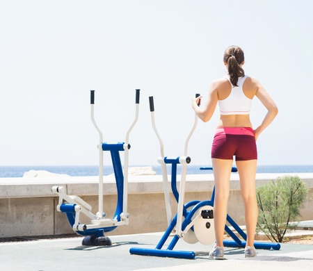 Fit and sporty woman training outside. Girl exercising on a sport machine in outdoor gym.の写真素材