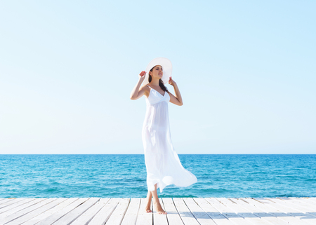 Woman in white dress on a wooden pier on summer.  Sea and sky background. Vacation, traveling and freedom concept.の写真素材