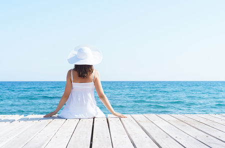 Woman in white dress on a wooden pier on summer.  Sea and sky background. Vacation, traveling and freedom concept.の写真素材