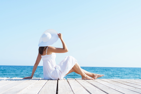 Woman in white dress on a wooden pier on summer.  Sea and sky background. Vacation, traveling and freedom concept.の写真素材