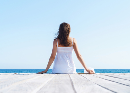 Woman in white dress on a wooden pier on summer.  Sea and sky background. Vacation, traveling and freedom concept.の写真素材