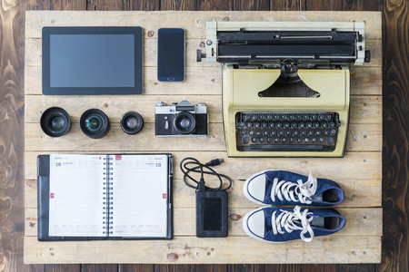 Outfit of a stylish traveler or a freelance journalist. Set of different objects and equipment: tablet, phone, organaizer, glasses, camera, lenses, hard drive, gumshoes, and typing machine.の写真素材