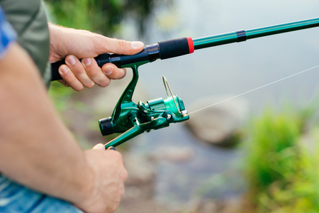 Fisherman with a spinning rod catching fish on a river. Man on a weekend. Hobby, leisure and active summer and autumn concept. Nature background.の写真素材