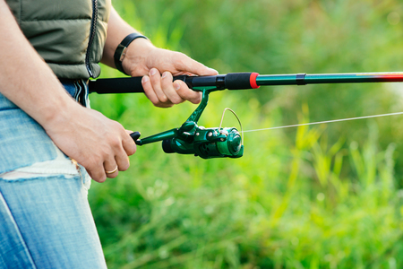 Fisherman with a spinning rod catching fish on a river. Man on a weekend. Hobby, leisure and active summer and autumn concept. Nature background.の写真素材