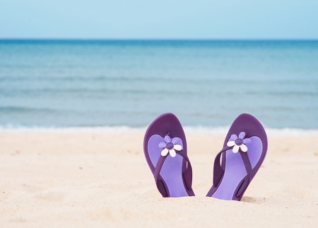 Beautiful, purple flip-flops on the beach on a sea background.の写真素材
