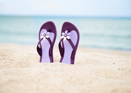 Beautiful, purple flip-flops on the beach on a sea background.の写真素材