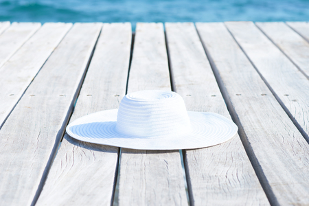 White hat on a wooden pier on summer.  Sea and sky background. Vacation, traveling and freedom concept.の写真素材
