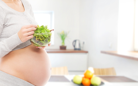 Woman expecting a baby. Pregnant belly closeup. Kitchen with window.の写真素材