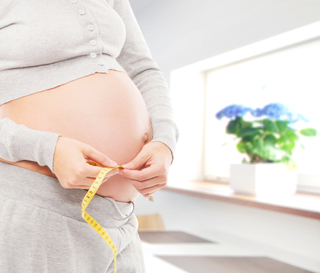 Woman expecting a baby. Pregnant belly close-up. Kitchen with window.の写真素材