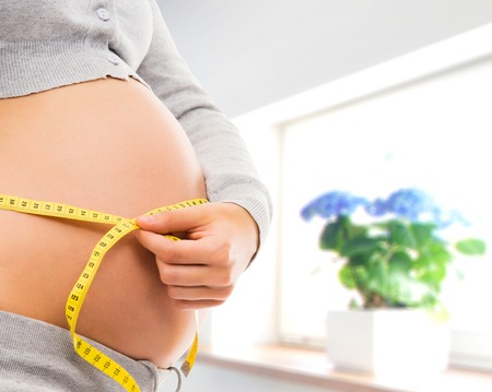 Woman expecting a baby. Pregnant belly close-up. Kitchen with window.の写真素材