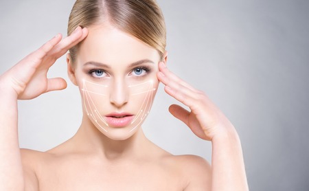 Portrait of attractive woman with smooth skin and beautiful, blue eyes over grey background. Face lifting concept.の写真素材