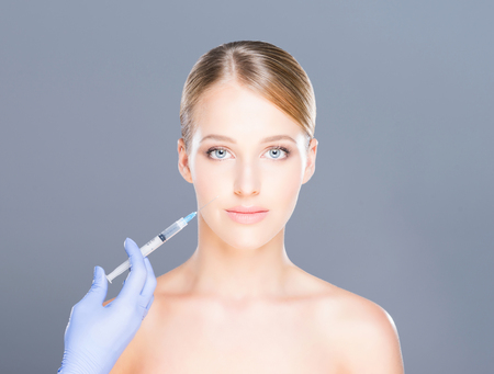 Doctor injecting botox in a beautiful face of a young woman. Plastic surgery concept.の写真素材