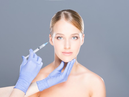 Doctor injecting botox in a beautiful face of a young woman. Plastic surgery concept.の写真素材