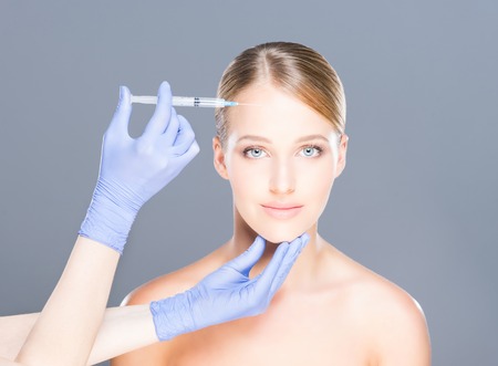Doctor injecting botox in a beautiful face of a young woman. Plastic surgery concept.の写真素材