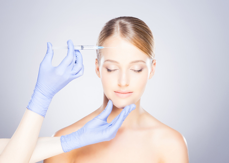 Doctor injecting in a beautiful face of a young woman. Plastic surgery concept.の写真素材