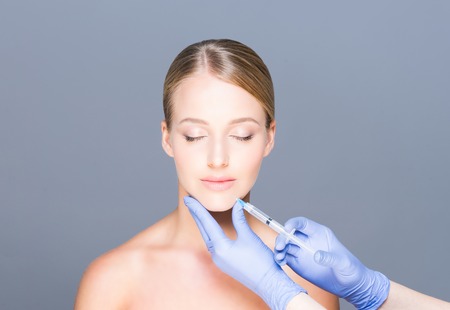 Doctor injecting botox in a beautiful face of a young woman. Plastic surgery concept.の写真素材