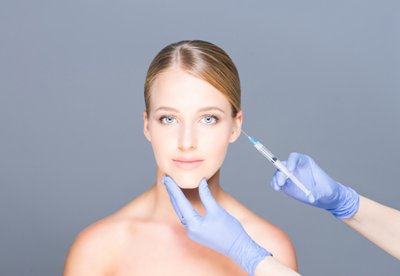 Doctor injecting botox in a beautiful face of a young woman. Plastic surgery concept.の写真素材
