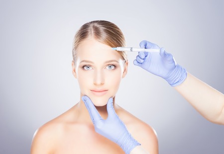 Doctor injecting in a beautiful face of a young woman. Plastic surgery concept.の写真素材