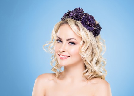 Beauty portrait of attractive blond girl with curly hair and a beautiful headband over blue background.の写真素材