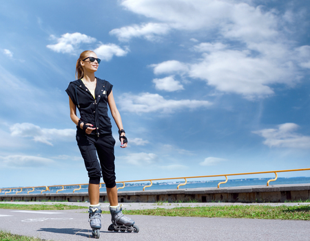 Young, beautiful and fit girl over sky background. Sporty woman rollerblading on skates.の写真素材