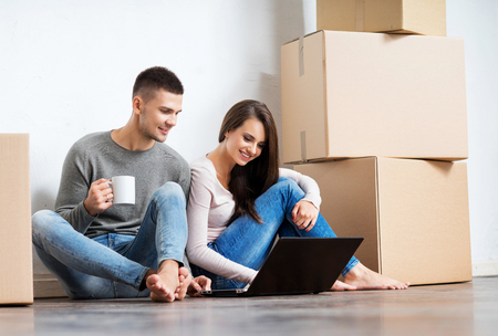 Young couple moving in a new home. Man and woman with notebook laptop computer and boxes.の写真素材