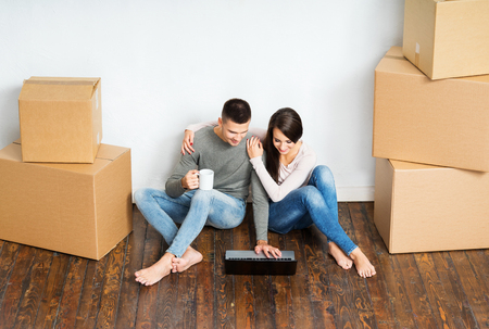 Young couple moving in a new home. Man and woman with notebook laptop computer and boxes.の写真素材