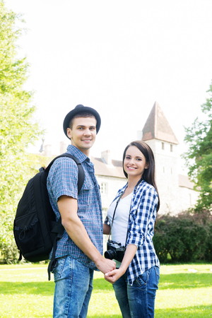 Beautiful traveling couple holding hands in summer park with medieval tower on the background.の写真素材
