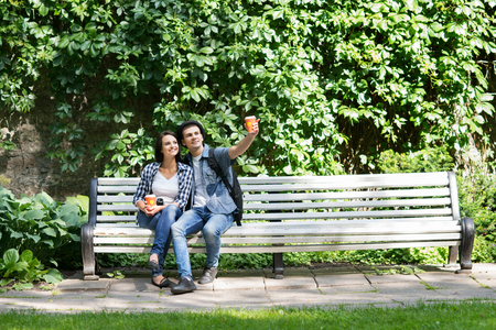 Beautiful young couple sitting on the bench with a cup of coffee in summer time.の写真素材