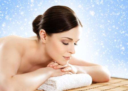 Beautiful, young and healthy woman in winter spa salon. Massage treatment over Christmas background with snow. Traditional medicine and healing concept.の写真素材