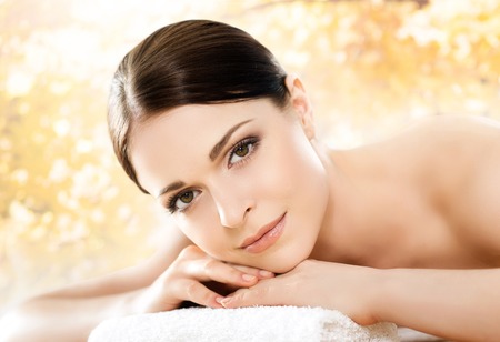 Young and beautiful girl relaxing in spa salon. Massage therapy over seasonal autumn background. Healing medicine and health care concept.の写真素材
