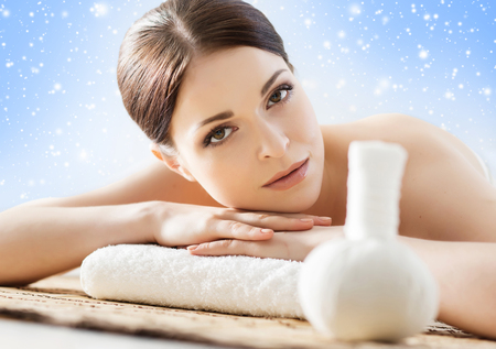 Young and beautiful girl relaxing in Christmas spa salon. Massage therapy over seasonal winter background with snowflakes. Healing medicine and health care concept.の写真素材