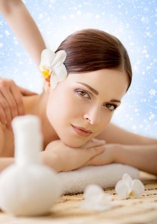 Beautiful, young and healthy woman in winter spa salon. Massage treatment over Christmas background with snow. Traditional medicine and healing concept.の写真素材