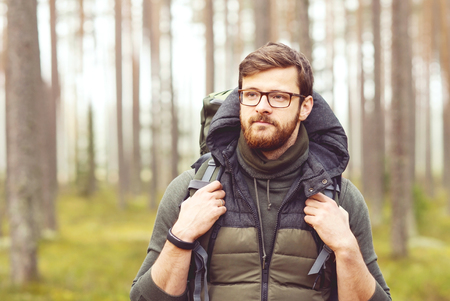 Camp, adventure, traveling concept. Man with a backpack and beard hiking in forest. Autumn color and hipster filter.の写真素材