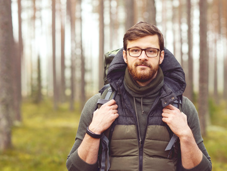 Camp, adventure, traveling concept. Man with a backpack and beard hiking in forest. Autumn color and hipster filter.の写真素材