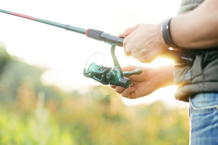 Fisherman with a spinning rod catching fish in a river. Man on a weekend. Hobby, leisure and active summer and autumn concept. Nature background.の写真素材