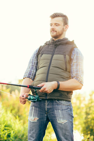 Fisherman with a spinning rod catching fish in a river. Man on a weekend. Hobby, leisure and active...